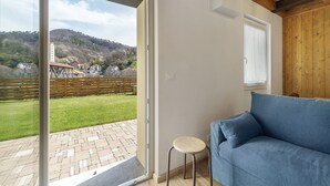 Une pièce avec un canapé bleu, un petit tabouret et une porte-fenêtre coulissante donnant sur une terrasse d’où l’on peut admirer un paysage vallonné.