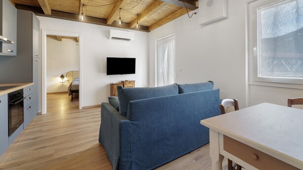 Un intérieur moderne avec un plafond en bois, un téléviseur à écran plat, un canapé bleu, une table à manger et un coin cuisine.