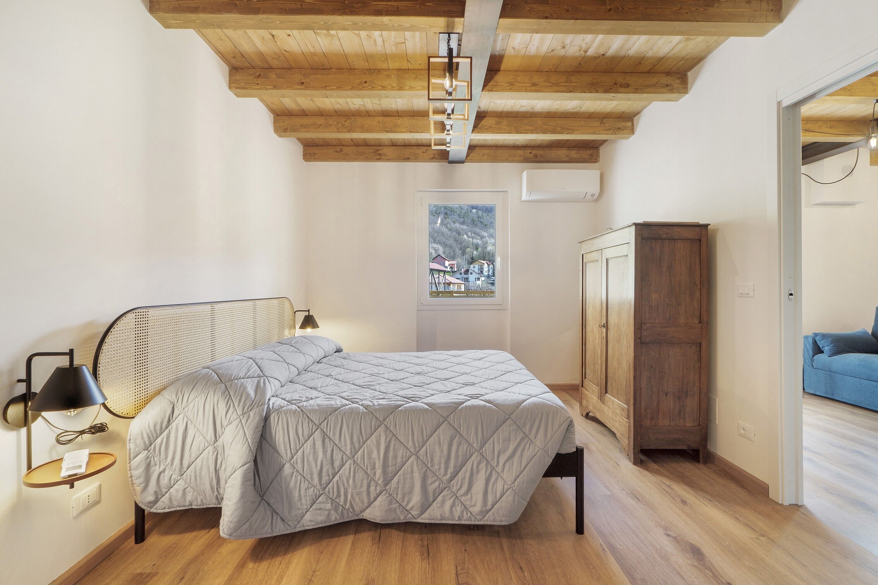 Una camera da letto con un letto, un armadio in legno, una finestra vista e una porta che conduce in un'altra stanza.