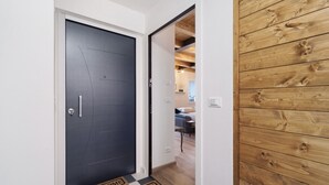 Un couloir avec une porte sombre, un paillasson et un lambris en bois sur le côté droit.