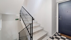 Un escalier avec des rampes noires menant à une porte sur laquelle est posé un paillasson avec l’inscription « BIENVENUE ».