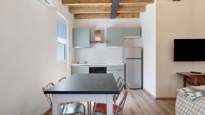 Une cuisine compacte dotée d’appareils électroménagers modernes, une table à manger avec des chaises et un téléviseur à écran plat fixé au mur.