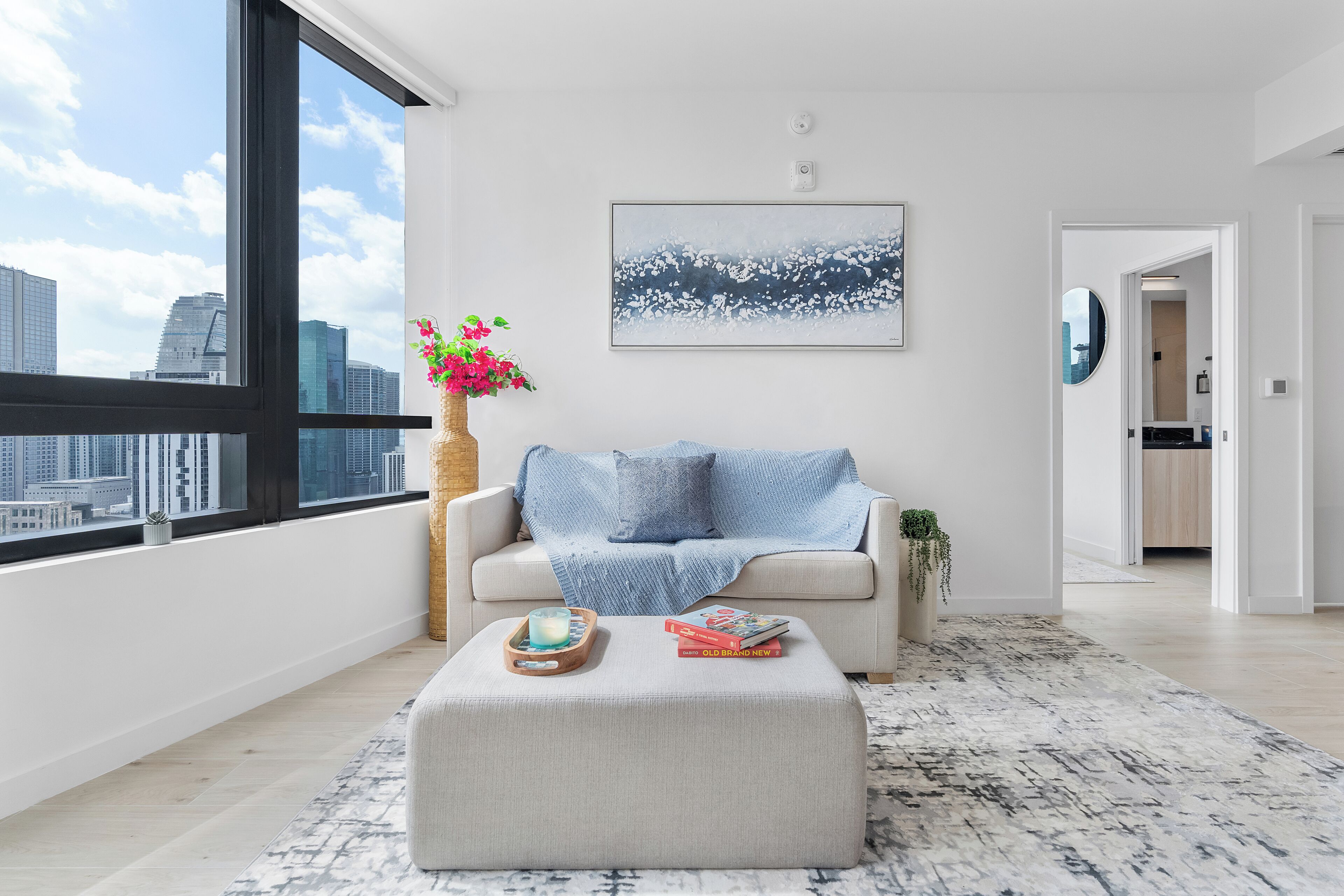 A modern living room with a large window, a sofa, a coffee table, and a painting on the wall.