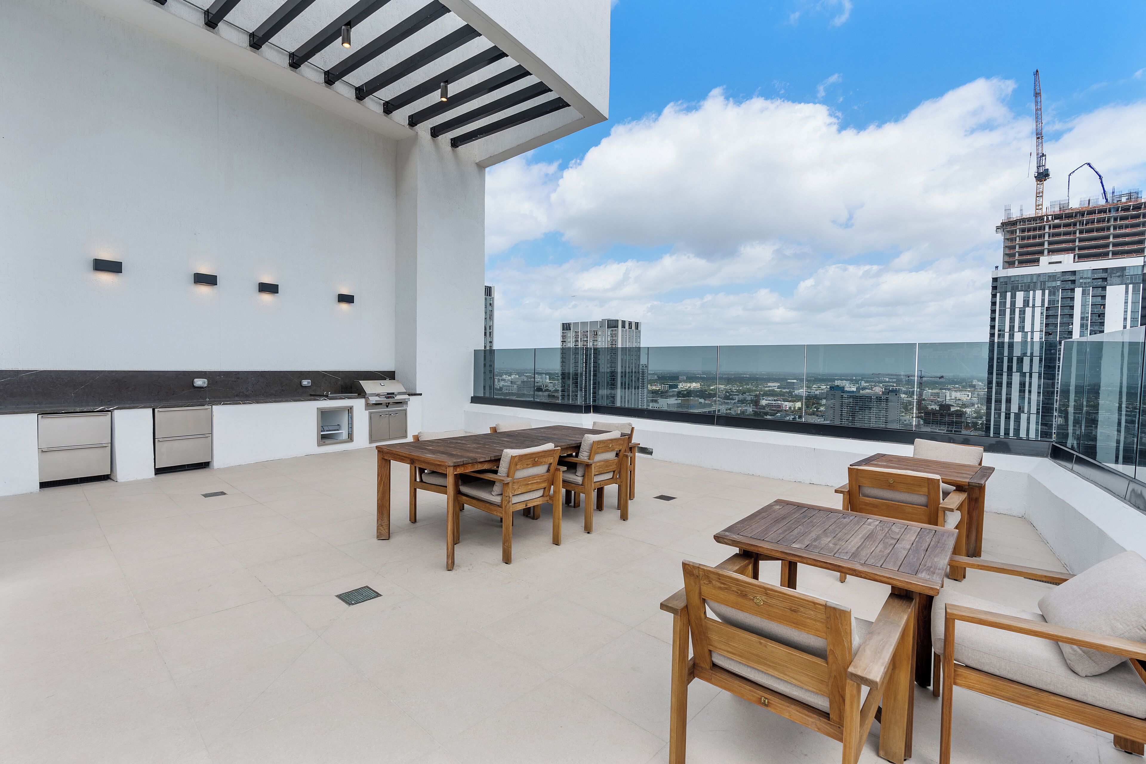 A rooftop terrace with wooden furniture, a kitchen area, and a city view.