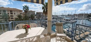 A balcony with a table, chairs, a flower vase, and a view of a marina with boats and buildings. - Sea View Apartment in  Fréjus (Fréjus)