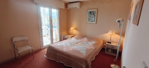 Ein Hotelzimmer mit Bett, zwei Nachttischen, einem Sessel und einem Fenster mit Aussicht. Eine Klimaanlage ist ebenfalls vorhanden.