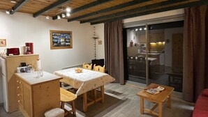 A dining area with a table and chairs, a small kitchen area, and a view through a glass door. - Apartment near the ski resort in Barcelonnette (Barcelonnette)