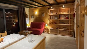 A cozy room with a wooden ceiling, a red sofa, a small table with a glass, and a bookshelf. - Apartment near the ski resort in Barcelonnette (Barcelonnette)