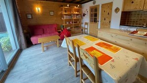 A cozy cabin interior with a wooden ceiling, a dining table with a quilt, a red sofa, and a bookshelf. - Apartment near the ski resort in Barcelonnette (Barcelonnette)