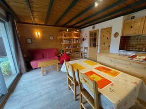 L’intérieur chaleureux d’un chalet avec un plafond en bois, une table à manger recouverte d’une courtepointe, un canapé rouge et une bibliothèque.