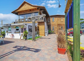Een houten gebouw met een balkon, een bordje waarop 'BEIGNETS & BREW' staat en een geplaveid gebied met plantenpotten.