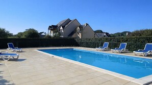 Piscina com espreguiçadeiras, deck revestido e um edifício ao fundo.