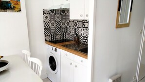 Cozinha compacta com máquina de lavar, pia e mesa branca com cadeiras.