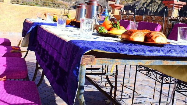 Una mesa al aire libre con montañas de fondo, un mantel y diversos alimentos.