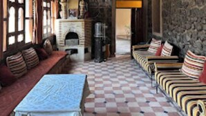 Una habitación acogedora con suelo a cuadros, vigas de madera en el techo y una chimenea, junto con una zona de estar con cojines estampados.