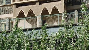 Un edificio con fachada de piedra, ventanas en arco y un balcón con gente.