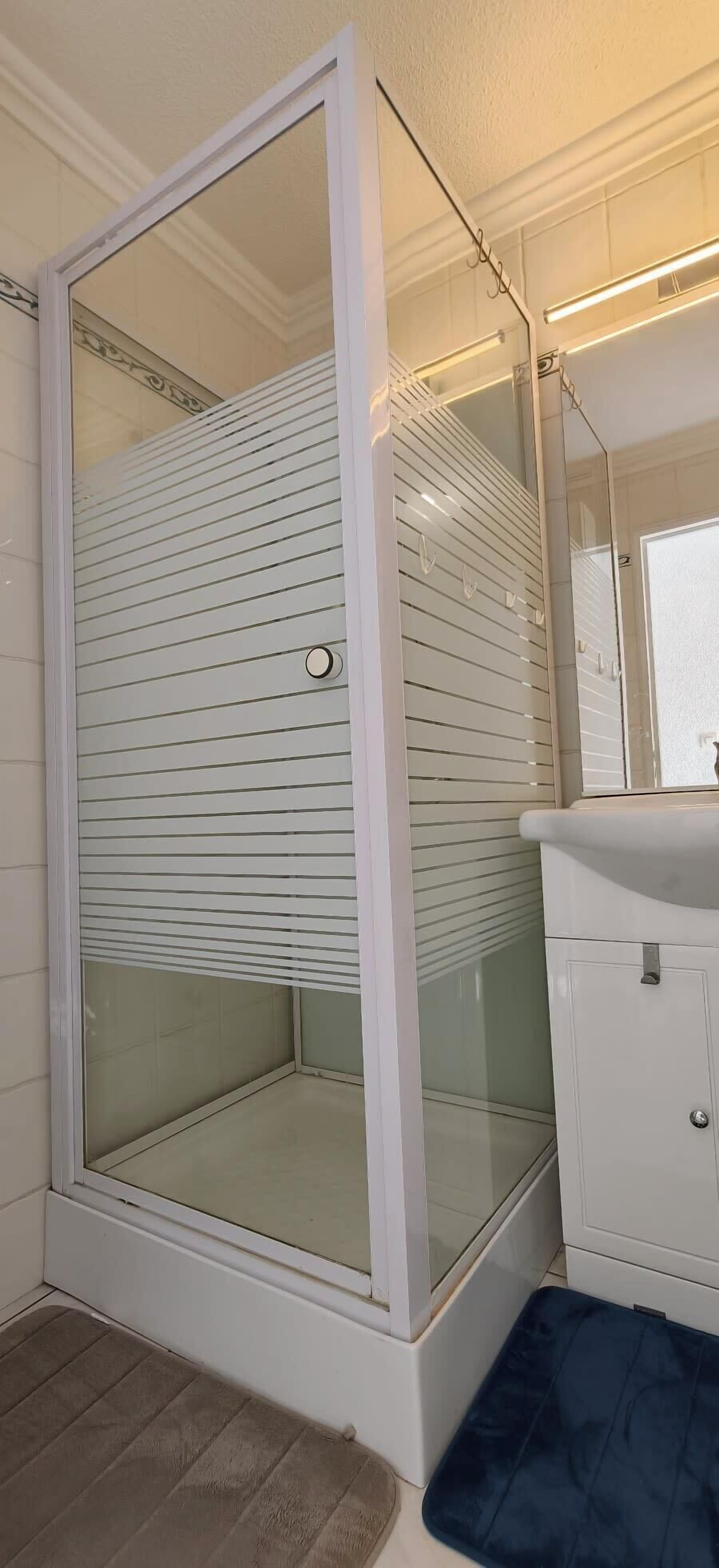 Une salle de bain avec une douche à parois de verre, un lavabo blanc et un miroir.