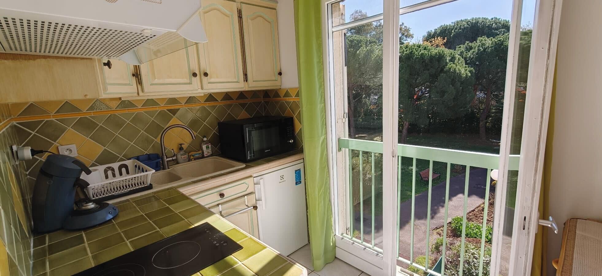 Une cuisine équipée d’un four à micro-ondes, d’un évier et offrant une vue sur un jardin grâce à une porte coulissante.