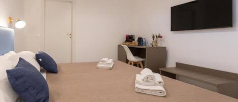 Un dormitorio con cama, escritorio, silla, televisor y puerta.