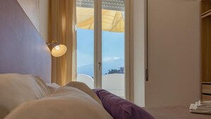 A bedroom with a bed, a nightstand, a lamp, and a view through a door. - Light View (Taormina)