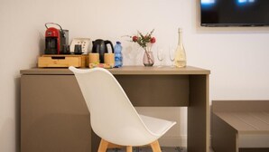 A modern room with a white chair, a wooden desk with a coffee maker, a kettle, a water bottle, a vase with flowers, and a bottle of wine. - Light View (Taormina)