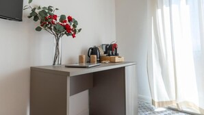 A small, modern room with a desk, a vase with red flowers, a coffee maker, and a window with sheer curtains. - Light View (Taormina)