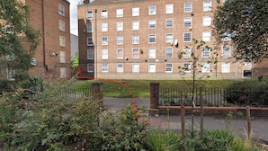 Un immeuble en briques de plusieurs étages, avec un jardin en premier plan.