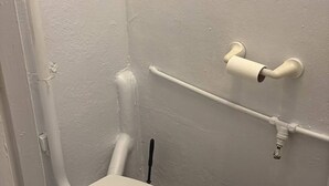 De petites toilettes blanches, avec une cuvette, un tuyau blanc et un mur blanc.