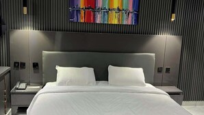 A modern hotel room with a large bed, a cityscape artwork on the wall, and two bedside lamps.