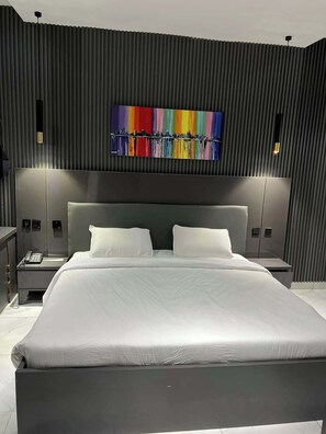 A modern hotel room with a large bed, a cityscape artwork on the wall, and two bedside lamps.