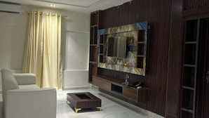 A modern living room with a white sofa, a coffee table, and a TV mounted on a wooden wall.