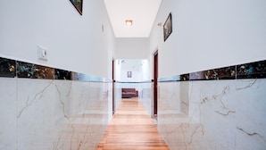 A hallway with marble walls and a wooden floor, leading to a room with a red sofa. - Suite Gm Comforts (Bengaluru)