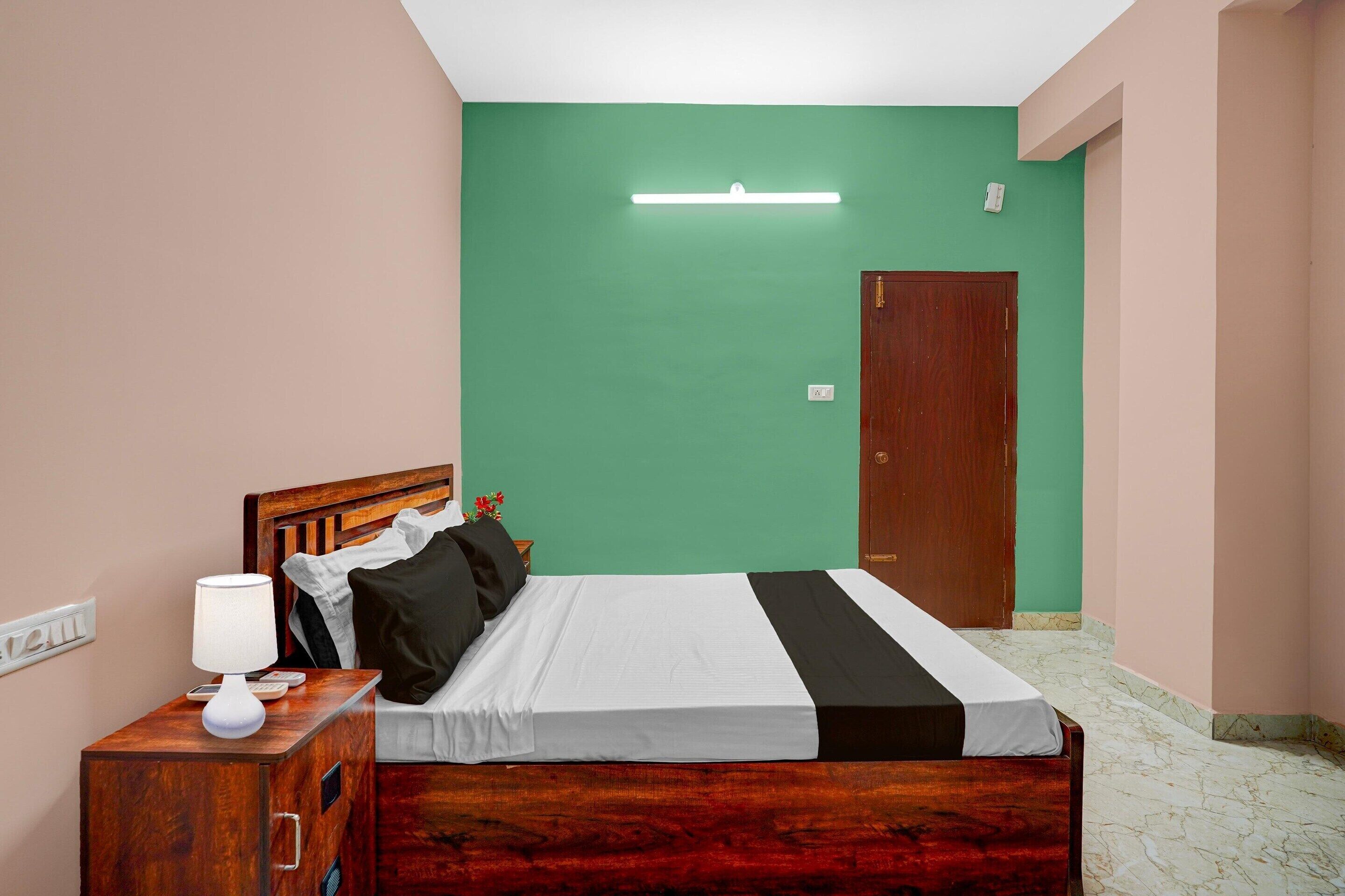 Un dormitorio ordenado con cama, mesita de noche, lámpara y una pared verde.