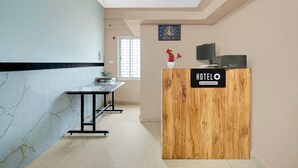 A hotel reception area with a wooden reception desk, a computer, and a vase with flowers. - Suite Gm Comforts (Bengaluru)