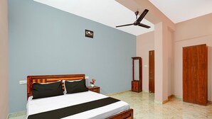 A bedroom with a bed, a nightstand, a mirror, a wardrobe, and a ceiling fan. - Suite Gm Comforts (Bengaluru)