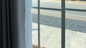 A view through a window with a building in the background, a road, and a landscaped area with bushes and flowers. - Siriwan boutique hotel (Takua Thung)