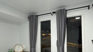 A hotel room with a bed, a window with curtains, a night view outside, and a small table with a basket and bottles. - Siriwan boutique hotel (Takua Thung)