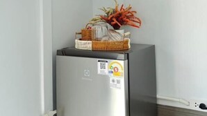 A compact refrigerator with a QR code sticker, a small basket with decorative items, and a power cord. - Siriwan boutique hotel (Takua Thung)