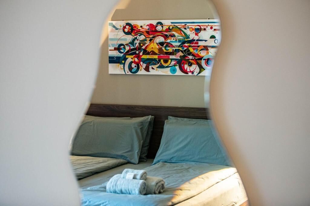 A hotel room with a bed, pillows, and a colorful abstract painting on the wall.