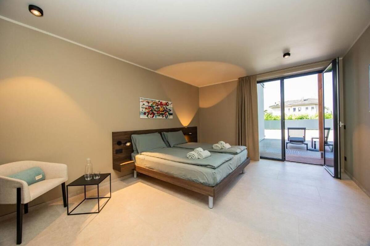 A modern bedroom with a bed, a bedside table, a chair, and a view of the outside.