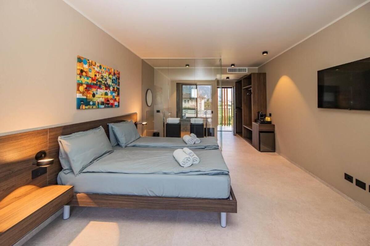 A modern hotel room with two beds, a TV, a painting, and a view of the outside.