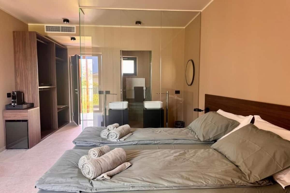 A hotel room with two beds, a small desk, a mirror, and a view of the outside.