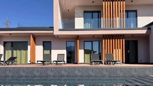 A modern hotel with a swimming pool, lounge chairs, and a balcony with wooden slats. - Vinea Rural Resort (Arco)