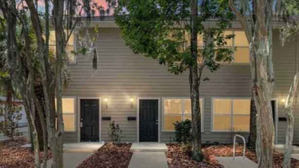 A two-story building with a symmetrical facade, a central entrance, and a small front yard with trees and a pathway. - Amazing Townhome - Premier Location. Adjacent to The Swamp. Parking. Comfortable (Gainesville)