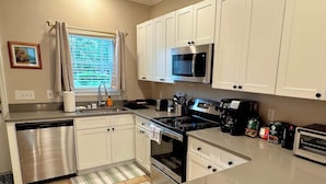 A kitchen with white cabinets, stainless steel appliances, and a window with curtains. - Amazing Townhome - Premier Location. Adjacent to The Swamp. Parking. Comfortable (Gainesville)