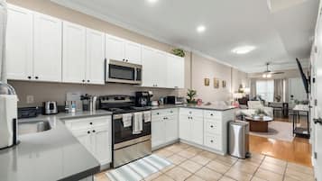 Una cocina moderna con armarios blancos, electrodomésticos de acero inoxidable y piso de baldosas.