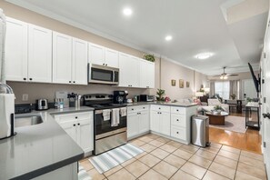 Una cocina moderna con armarios blancos, electrodomésticos de acero inoxidable y piso de baldosas.