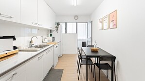 Una cocina moderna con armarios blancos, encimera negra, un fregadero, microondas y una zona de comedor con mesa y sillas negras.