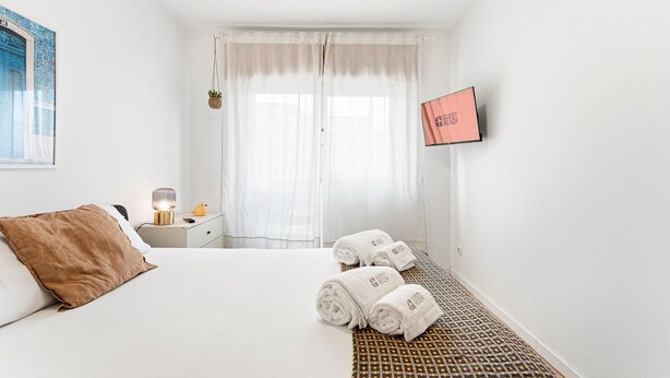 Habitación de hotel con una cama, una mesita de noche con lámpara, un televisor y una ventana con cortinas.