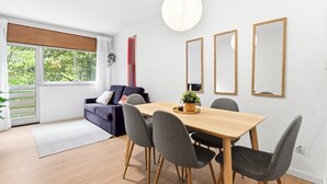 Una sala de estar moderna con una mesa de comedor, sillas grises, un sofá y un ventanal con vistas a zonas verdes.